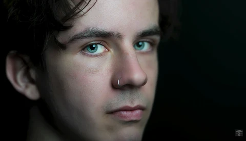 Close-up portrait of a man with striking turquoise eyes against a dark background.