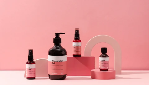 Product display with five dark glass bottles and containers arranged on pink geometric platforms against a pink background.