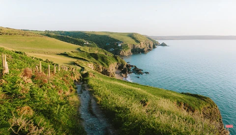 Coastal hillside with green pasture sloping toward turquoise ocean and rocky headlands.