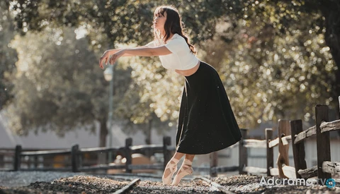 Ballet dancer in pointe shoes performing an arabesque outdoors under golden tree foliage.