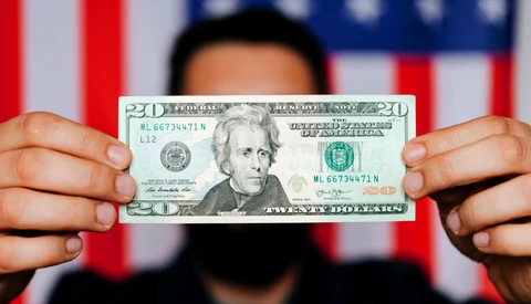 Hands holding a twenty-dollar bill against an American flag background.