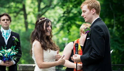 Bride and groom exchange vows during outdoor wedding ceremony with officiant and groomsman present.