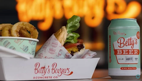 Onion rings and burger in branded paper containers with a beer can on dark background with warm bokeh lighting.