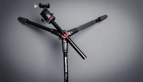Professional tripod with three extended legs and ball head with smartphone mount against gray background.