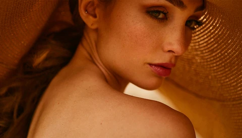 Woman's face and bare shoulder against warm, textured background with dramatic side lighting.