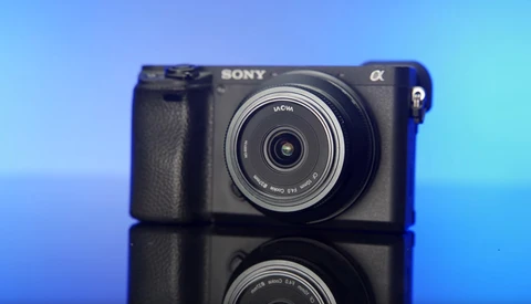 Sony Alpha mirrorless camera with wide-angle lens mounted, positioned against blue gradient background with reflection.