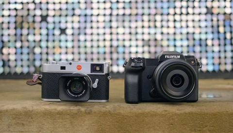 A rangefinder film camera and a mirrorless digital camera displayed side by side on a wooden surface.