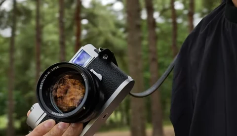 Vintage rangefinder camera with standard lens held in hand outdoors with trees in background.