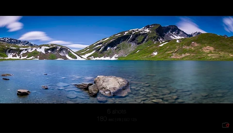 Alpine lake with turquoise water, rocky shores, and snow-capped mountain peaks under blue sky.