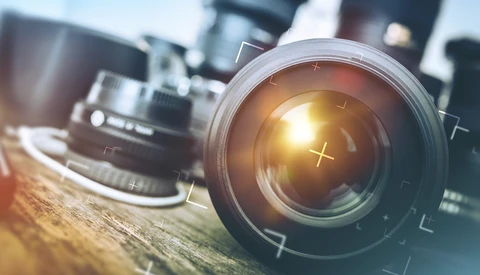 Multiple camera lenses arranged on a wooden surface with golden hour sunlight reflecting off the front element of the closest lens.