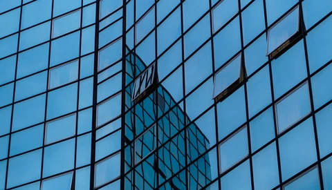Modern glass skyscraper facade with geometric grid pattern and reflective building silhouette.