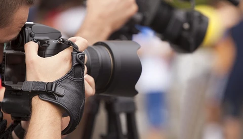Photographer holding a DSLR camera with telephoto lens at an outdoor event.