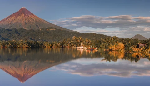 Conical volcano with perfect mirror reflection in still lake at golden hour.