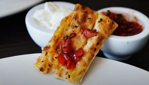 Toasted bread slice topped with melted cheese and red peppers, served with white dipping sauces and a red condiment bowl.