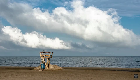 Wooden lifeguard tower on an empty beach under a dramatic cloudy sky.
