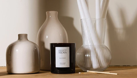 Minimalist still life arrangement with ceramic vessels, a black candle, and glass vases on a wooden surface.