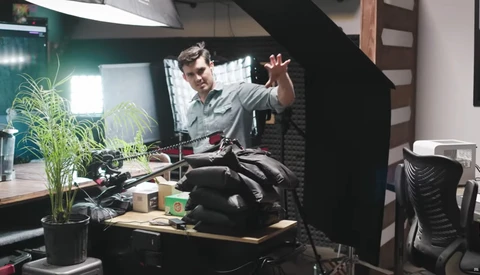 Podcaster gesturing while speaking into a microphone in a home studio setup.