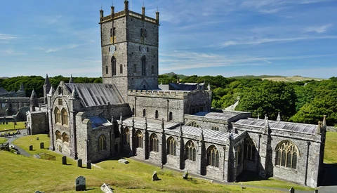 Medieval stone cathedral with square tower surrounded by graveyard, shot under blue sky with green landscape.