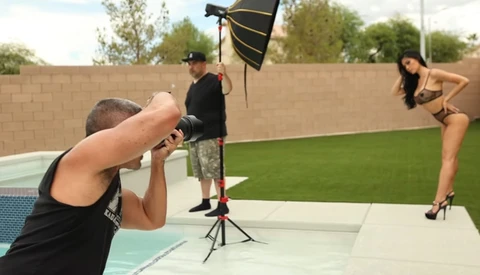 Photographer using a camera on a residential patio with studio lighting and reflectors during a fashion shoot.