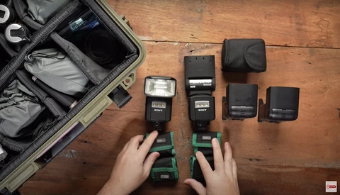 Photography gear laid out on wooden surface with camera flashes, battery packs, and equipment case.