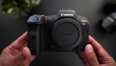 Canon EOS R5 mirrorless camera held in hands, body only, against blurred background.