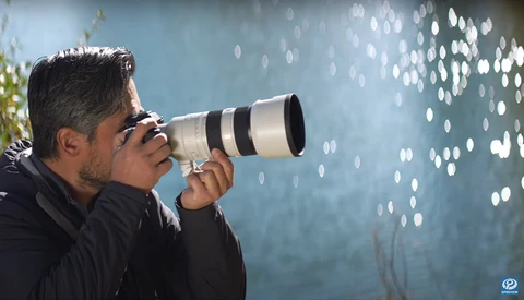 Photographer holding telephoto lens pointed at bokeh lights against blue background.
