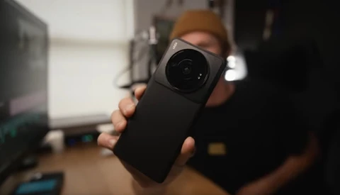 Person holding a smartphone with a large camera lens attachment toward the viewer.