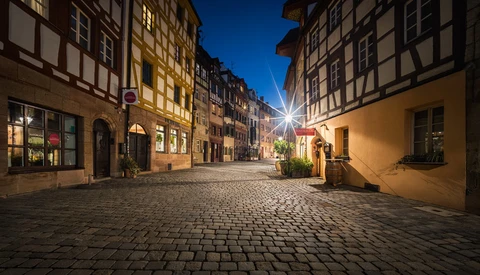 Illuminated cobblestone street lined with half-timbered buildings at dusk in a historic European town.