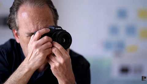 Photographer holding a Canon camera to his eye, composing a shot with focused concentration.