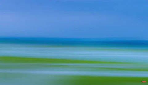 Horizontal bands of blue sky, turquoise water, and green seaweed or algae in calm coastal waters.