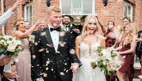 Newlyweds walk together while guests throw gold confetti during outdoor wedding recessional.