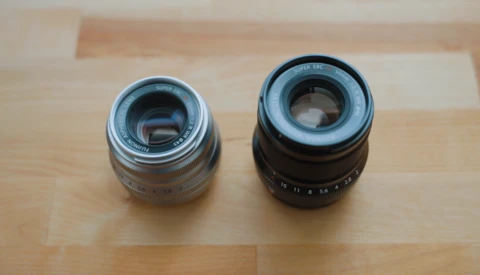 Two vintage camera lenses placed side-by-side on a wooden surface for comparison.