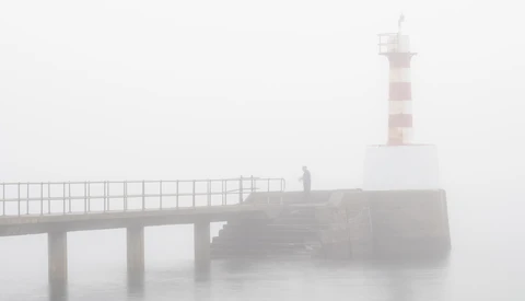 Lighthouse and pier shrouded in thick fog, minimalist coastal scene.