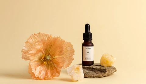 Orange poppy flower beside amber dropper bottle and crystals on weathered wood against cream background.