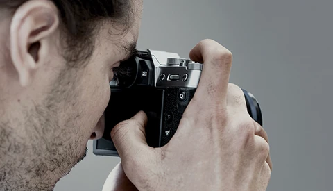 Photographer holding a mirrorless camera up to his eye while composing a shot.