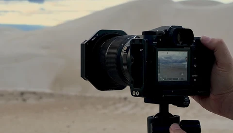 Mirrorless camera with wide-angle lens mounted on tripod, held in hand during outdoor desert shoot.