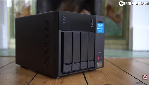 Black desktop NAS storage device with four drive bays positioned on a wooden table.