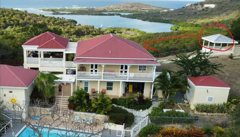 Aerial view of a large residential property with red metal roofs overlooking a coastal bay and forested hillside.
