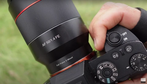 Hand holding a mirrorless camera with an AF 60/1.4 FE lens mounted, showing manual focus and exposure controls.