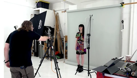 Photographer adjusting lighting setup while model poses in studio during portrait session.