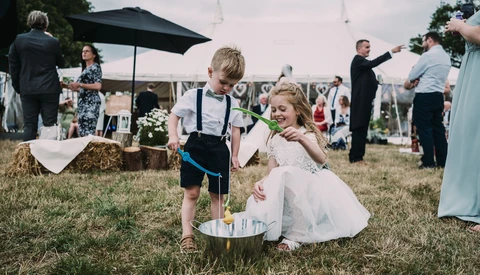 Two young children playing in a sandbox at an outdoor garden wedding ceremony.