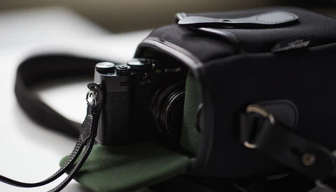 Compact rangefinder camera with black leather strap on olive green fabric bag.