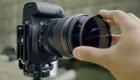 Photographer's hand adjusting a wide-angle lens on a cinema camera mounted on a tripod.
