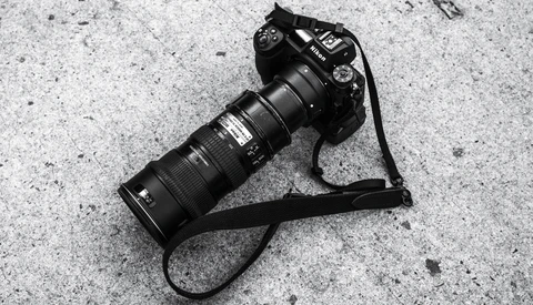 Professional DSLR camera with telephoto lens on concrete surface with neck strap.
