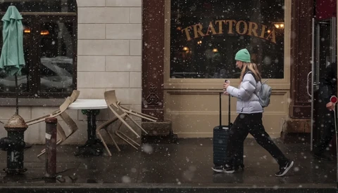 Person jogging past a trattoria storefront during heavy snowfall in an urban setting.