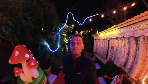 Man posing with neon blue lightning bolt and glowing red mushroom decorations at night.