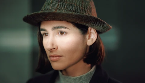 Portrait of a person wearing a tweed fedora and turtleneck sweater, looking to the side.