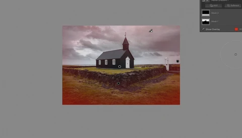 Isolated red-roofed church with white walls standing alone on russet terrain beneath dramatic clouded sky.