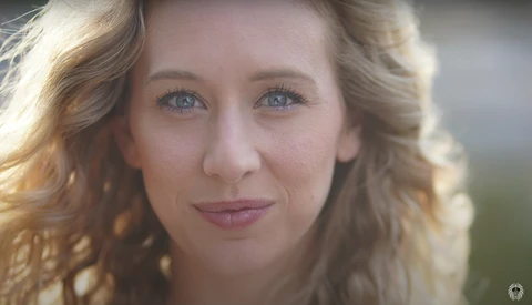 Woman with wavy blonde hair and blue eyes in golden hour portrait lighting.