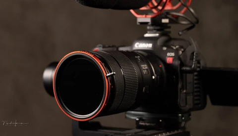 Canon EOS R5C mirrorless camera with Canon lens featuring red accent ring, mounted on tripod with directional microphone visible above.